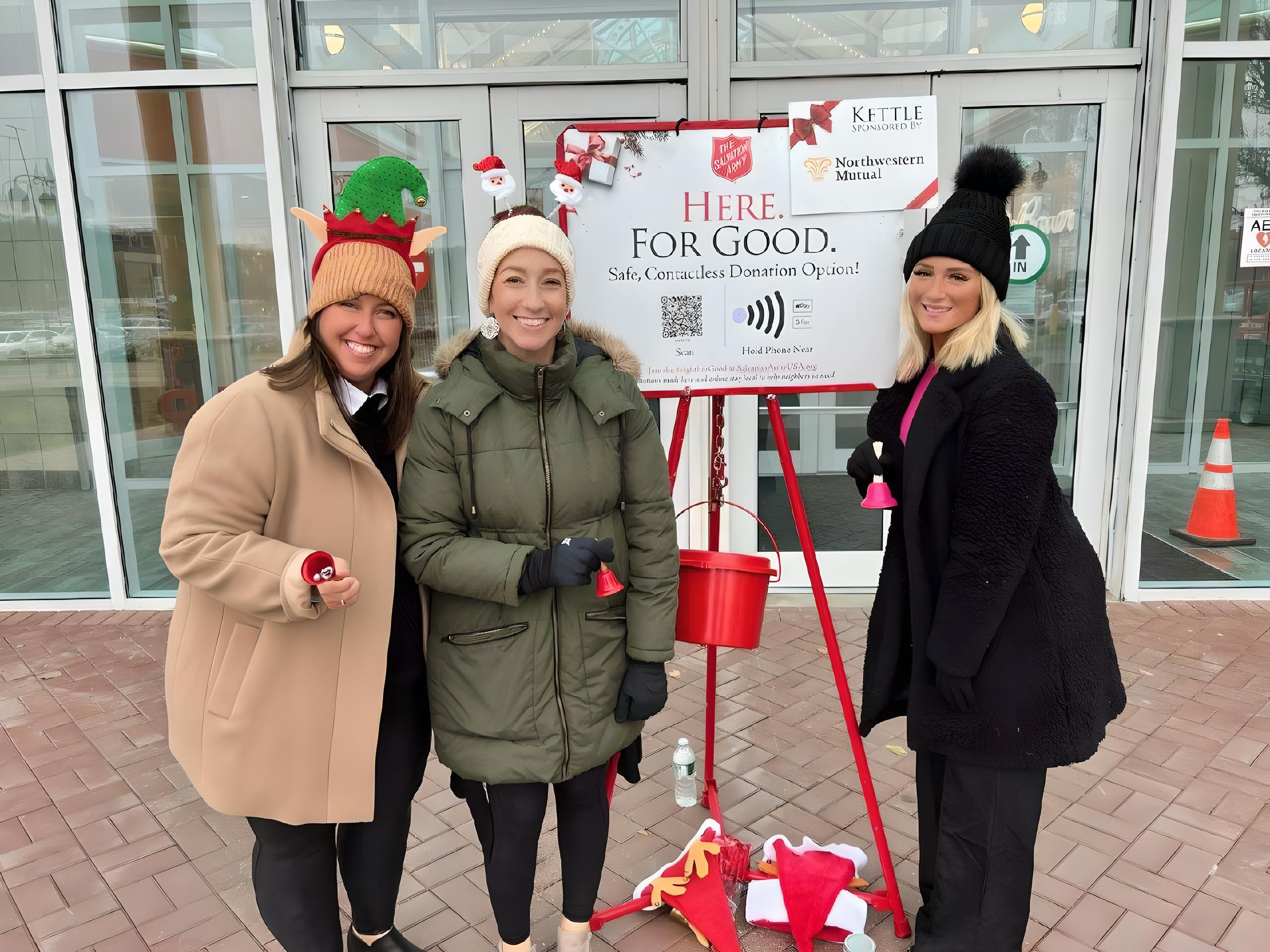 Three Rochester volunteers ringing bells beside a red kettle outside a local business